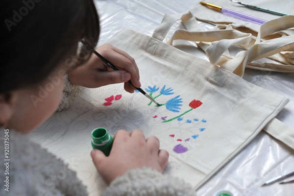 Fototapeta Child lefthander paints a canvas bag with acrylic paints.