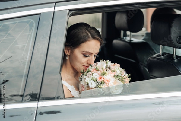Fototapeta A bride is sitting in a car with a bouquet of flowers in her lap. She is looking out the window, possibly lost in thought or admiring the scenery. Concept of romance and anticipation