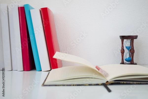 Fototapeta Books, hourglasses and open notebook on white table