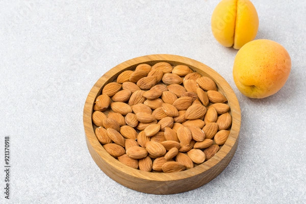 Fototapeta Apricot kernels in a wooden bowl and whole apricots on a light background. Horizontal free space.