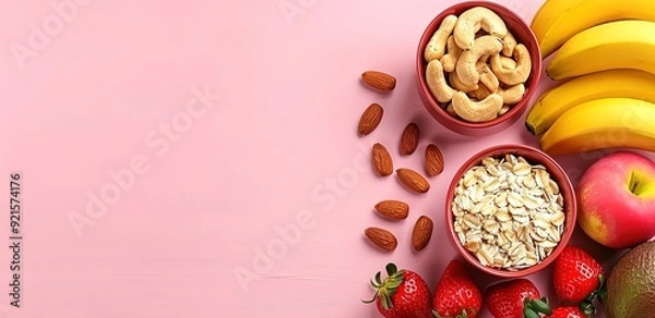 Fototapeta Two wooden bowls of almonds and oats with bananas, apples, and stawberries and almonds on a pink background