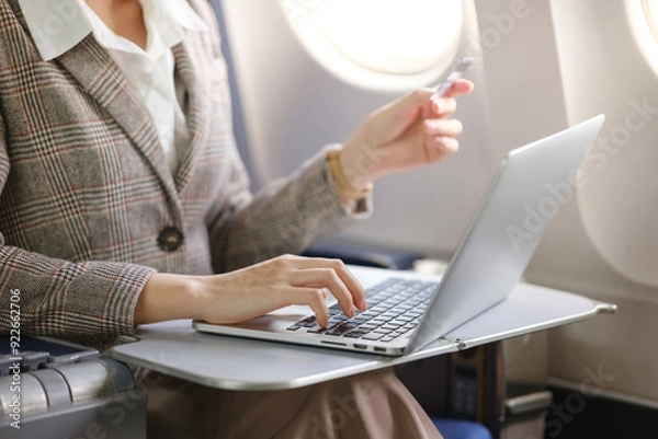 Fototapeta A woman is sitting on a plane with a laptop open in front of her