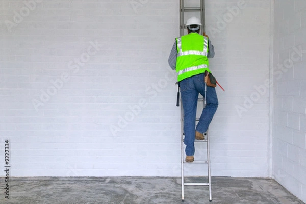 Fototapeta Workman in reflective vest and hard hat climbing a ladder