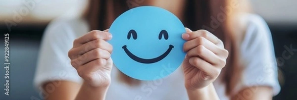 Obraz Embracing Positivity: A Woman Crafts a Joyful Smile on Blue Paper for World Mental Health Day, Symbolizing the Importance of Active Thinking and Psychological Well-being.