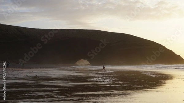 Obraz Surfer at Sunset on Scenic Beach with Coastal Arch in Morocco, Legzira Beach.
