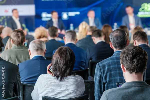 Fototapeta Audience members attentively listen to a panel discussion at a business conference, with focus on networking and knowledge sharing.