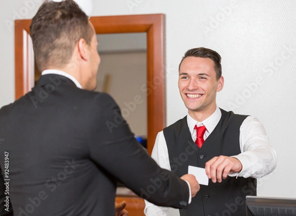 Fototapeta receptionist at hotel reception handing key card to guest