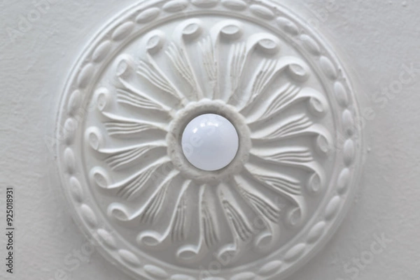 Fototapeta Energy-saving ceiling light bulb and ornamental round plasterboard cornice close-up.