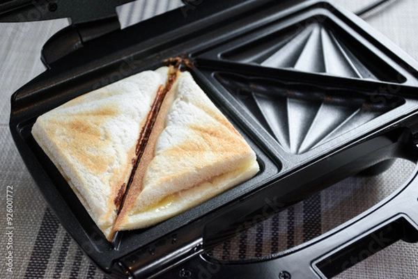 Obraz Close up of hot sandwich ham and cheese on a toaster for making hot sandwich toast breakfast. Bread and toaster on the kitchen table.