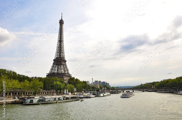 Obraz The Seine River in Paris with a historic bridge and the illuminated Eiffel Tower in the background. The calm water reflects the city lights, creating a romantic atmosphere of a Parisian evening