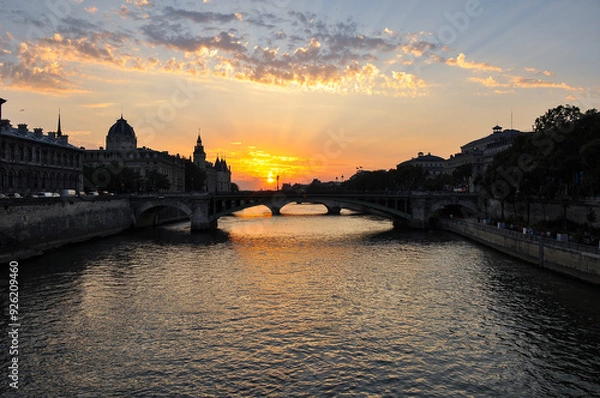 Fototapeta The Seine River in Paris with a historic bridge and the illuminated Eiffel Tower in the background. The calm water reflects the city lights, creating a romantic atmosphere of a Parisian evening