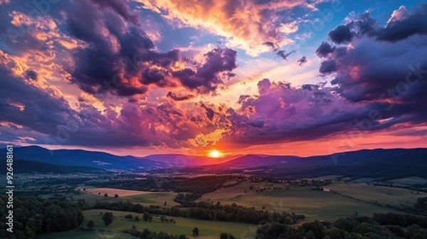 Fototapeta Amazing sunset with dramatic clouds illuminated in fiery colors above a peaceful rural landscape.