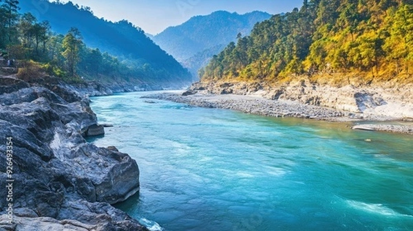 Fototapeta Ganges River in the foothills of the Himalayas, with clear blue water flowing through rocky terrain and forested banks.