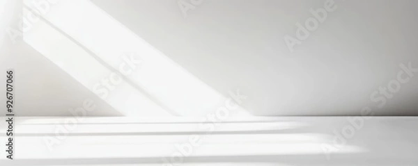 Fototapeta Minimalist white interior with natural light streaming through a window, casting geometric shadows on the smooth surface.
