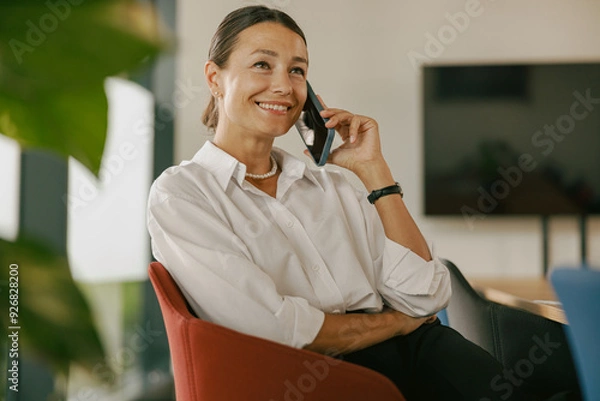Fototapeta A confident woman smiling and engaging in a phone conversation in a modern office