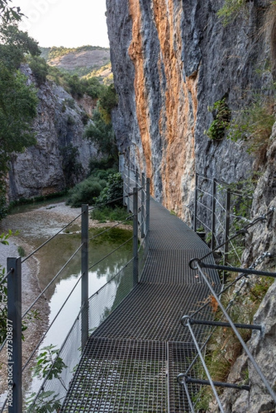 Fototapeta Iron walkways anchored to the side of the rock mountain and with river on the side
