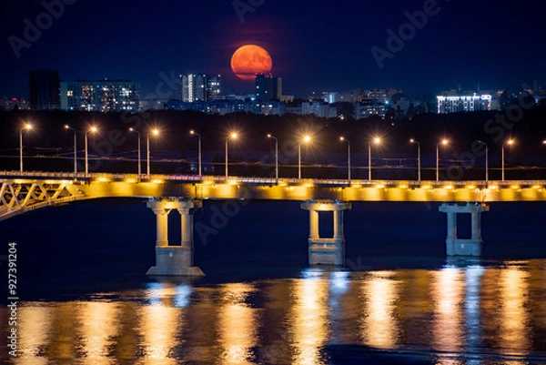 Fototapeta The full moon rises at night. The bridge over the Volga River between the cities of Saratov and Engels, Russia.