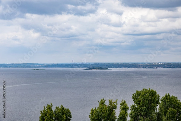 Fototapeta Summer river landscape. The horizon line, clouds in the sky, trees in the foreground.