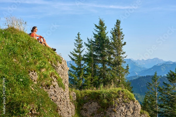 Fototapeta pretty senior woman hiking in warm dawn sunlight and enjoying the spectacular view over the Allgau alps on the Nagelfluh mountain chain near Oberstaufen, Bavaria, Germany