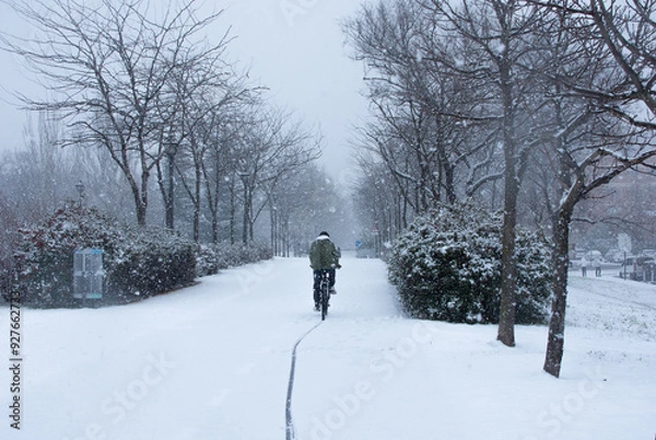 Fototapeta Cyclist riding on a snowy cycle path during a storm