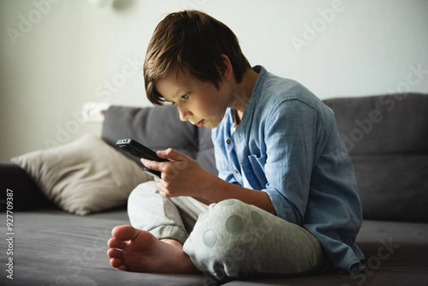 Fototapeta Boy with a serious face on the couch communicates on Internet. Child gadget addiction