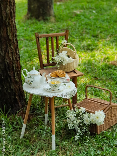 Fototapeta Chamomile flowers, books, glass teapot and cup with herbal tea on table in garden, natural background. summer season. relax time. useful calming tea. tea party outdoor