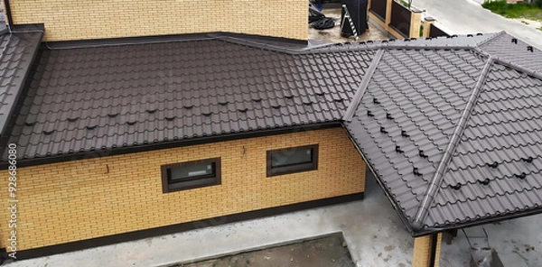 Fototapeta Close-up house roof with steel roofing sheet. Brown modular tile effect roof panel. Traditional metal shingle tiles. Profiled metallic corrugated pantile as clay or concrete slate. Building's covering