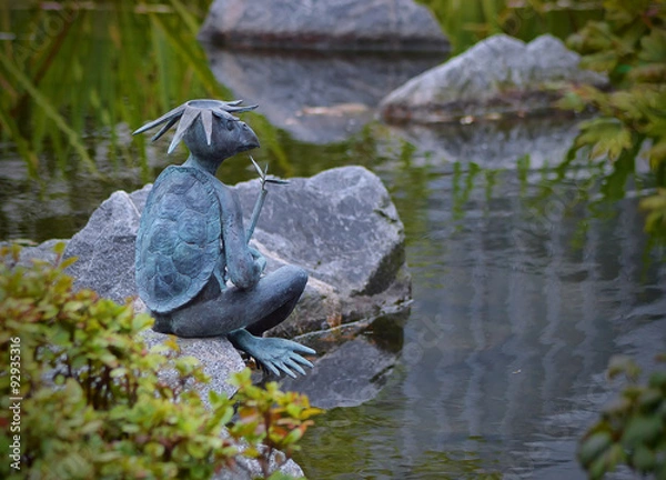 Obraz Бронзовая скульптура каппы сидящая на камне у пруда.