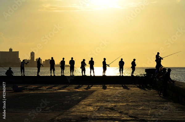 Fototapeta Every day, before sunset, dozens of fishermen meet in the Malecon (Havana's harbour, Cuba). Here you can observe some of them with their shadows, and the beautiful sunset in the background.