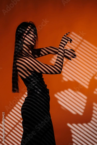 Fototapeta Brunette girl posing in a beam of light in the studio, on a red background, light and darkness.