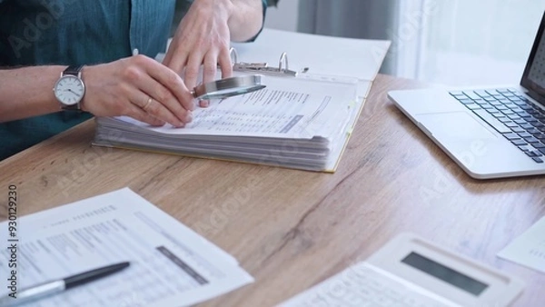 Fototapeta Businessman or auditor wearing green shirt is reviewing financial documents with magnifying glass. Business work process in bookkeeping office. Taxes