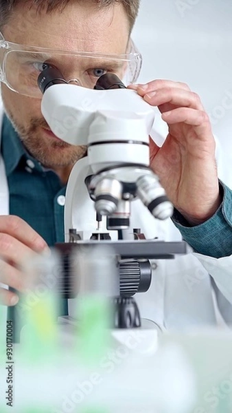Fototapeta Man scientist with protective glasses using microscope in laboratory. Microbiology science concept
