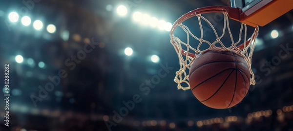 Fototapeta A basketball entering the hoop during a game in a brightly lit arena, focus on action and sportsmanship. copy space