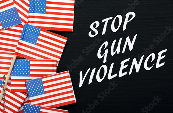 Fototapeta The words Stop Gun Violence in white text on a blackboard alongside miniature flags of the United States of America