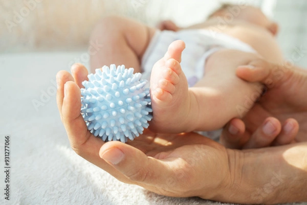 Fototapeta Dad making massage baby legs with a massage ball. Sensory, tactile development, activity muscles. Concept of taking care baby, fine motor skills. close up.