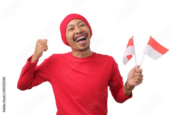 Obraz Excited Indonesian man in a red long sleeve T-shirt and beanie holds the Indonesian flag and raises his fist in celebration of Indonesian Independence Day on August 17, isolated on a white background