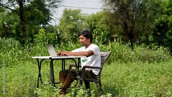 Fototapeta Indian young boy doing work from home. Man sitting on office table at garden doing work on internet