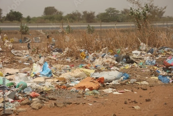 Obraz Vue rapprochée d'une décharge sauvage au Sénégal composée de déchets en plastique et d'emballages en carton et située près d'une route. Symbole de la pollution et de la dégradation de l'environnement.