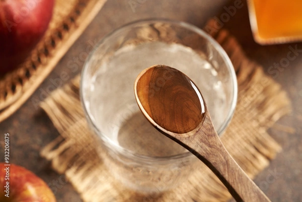 Fototapeta A spoonful of apple cider vinegar above a glass of water