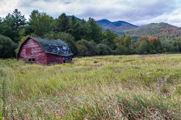 Fototapeta Old run down barn with fall color in the Adirondacks in the background