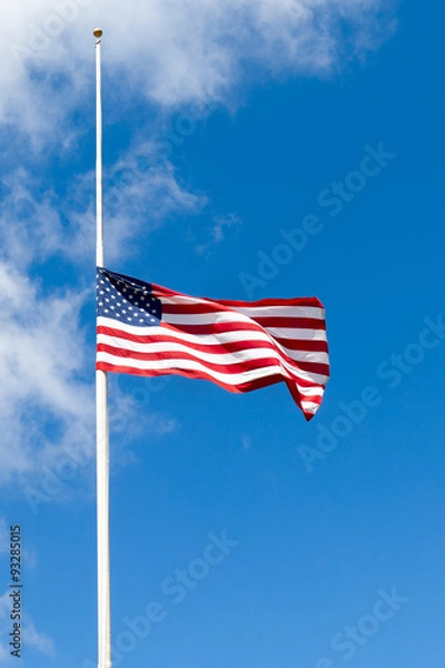 Obraz American flag flying at half mast against blue sky with white clouds. Copy space