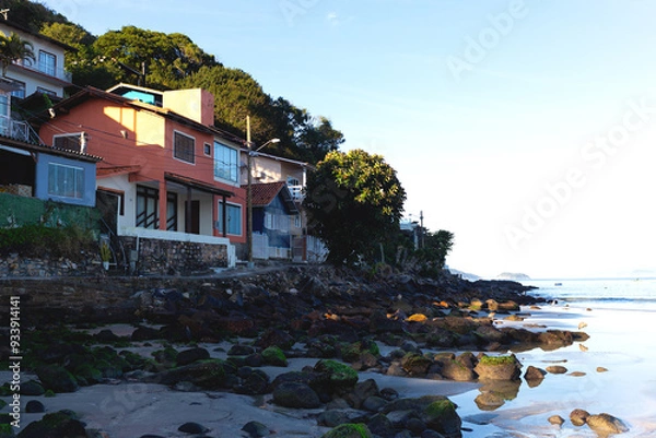 Fototapeta Colorful hillside village by the beach, surrounded by lush greenery and calm ocean waves