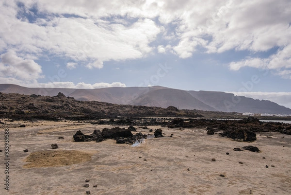 Fototapeta White sand beach with black rocks of volcanic origin. Mountains in the background and sky with big white clouds. Caletón Blanco, Lanzarote, Canary Islands, Spain