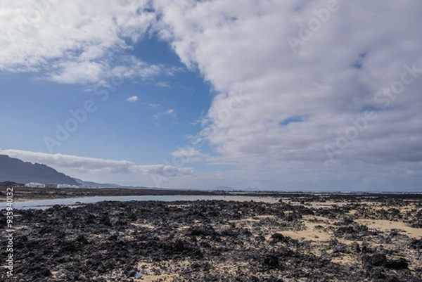Obraz White sand beach with black rocks of volcanic origin. Mountains in the background and sky with big white clouds. Caletón Blanco, Lanzarote, Canary Islands, Spain