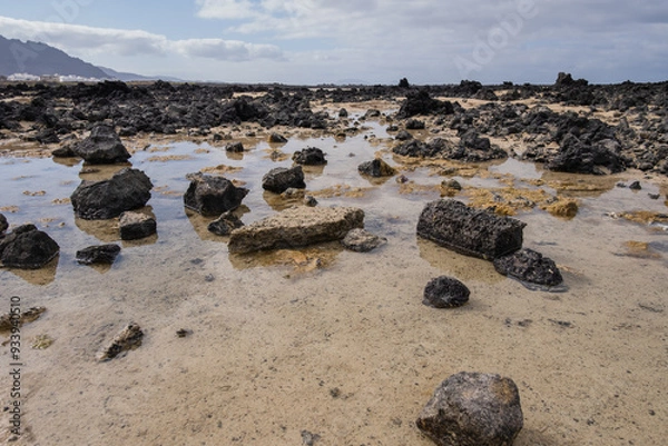 Fototapeta White sand beach with black rocks of volcanic origin. Mountains in the background and sky with big white clouds. Caletón Blanco, Lanzarote, Canary Islands, Spain