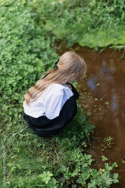 Obraz preschool girl stands on the bank of a stream and looks into the water
