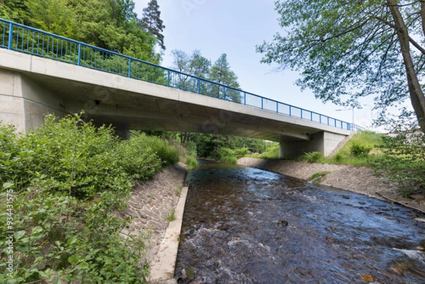 Fototapeta Reinforced concrete road bridge over the river. Close-up during sunny day in summer. Aerial view on a bridge across a small river. Canal or ditch with green grass meadow, Underneath of classic style 