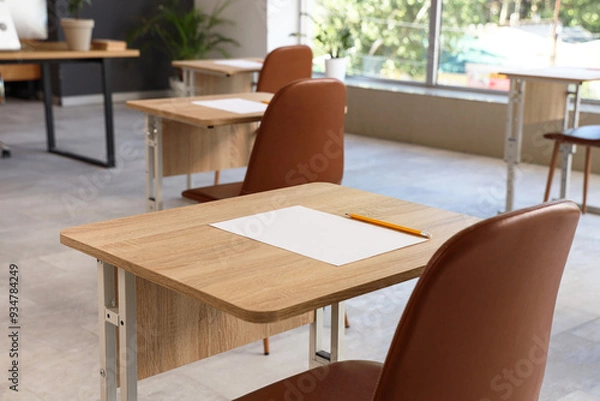 Fototapeta School desks with sheet of paper and pencil prepared for exam. Closeup