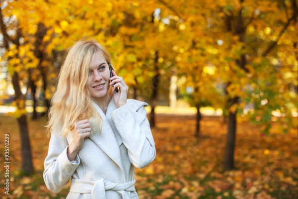 Fototapeta girl in white coat talking on the phone in the autumn park