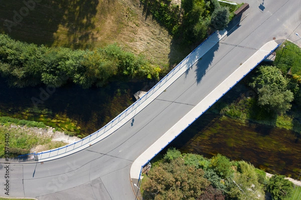 Fototapeta Reinforced concrete road bridge over the river. Close-up during sunny day in summer. Aerial view on a bridge across a small river. Canal or ditch with green grass meadow, Underneath of classic style 